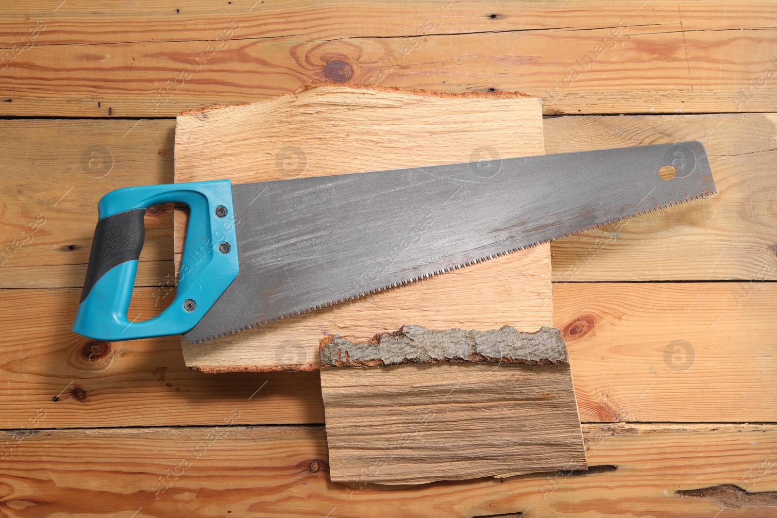 Photo of Saw with light blue handle and logs on wooden background, top view