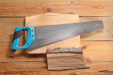 Photo of Saw with light blue handle and logs on wooden background, top view