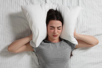 Photo of Irritated young woman covering her ears with pillow on bed, top view. Insomnia problem