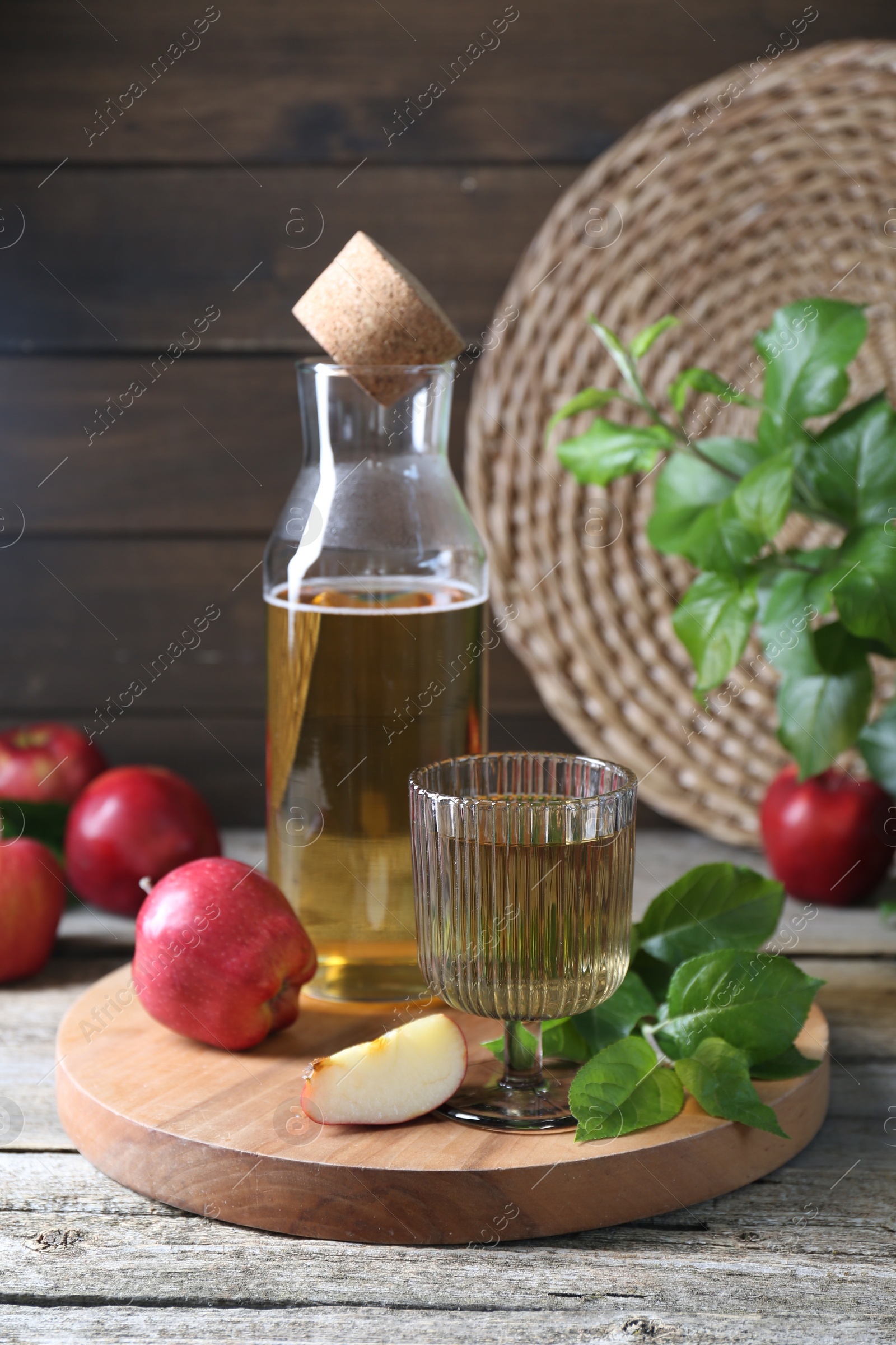 Photo of Delicious cider and apples with green leaves on wooden table