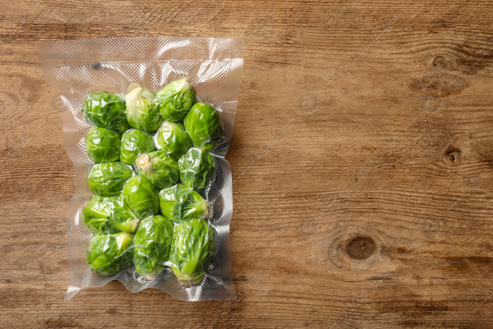 Photo of Vacuum pack of Brussels sprouts on wooden table, top view