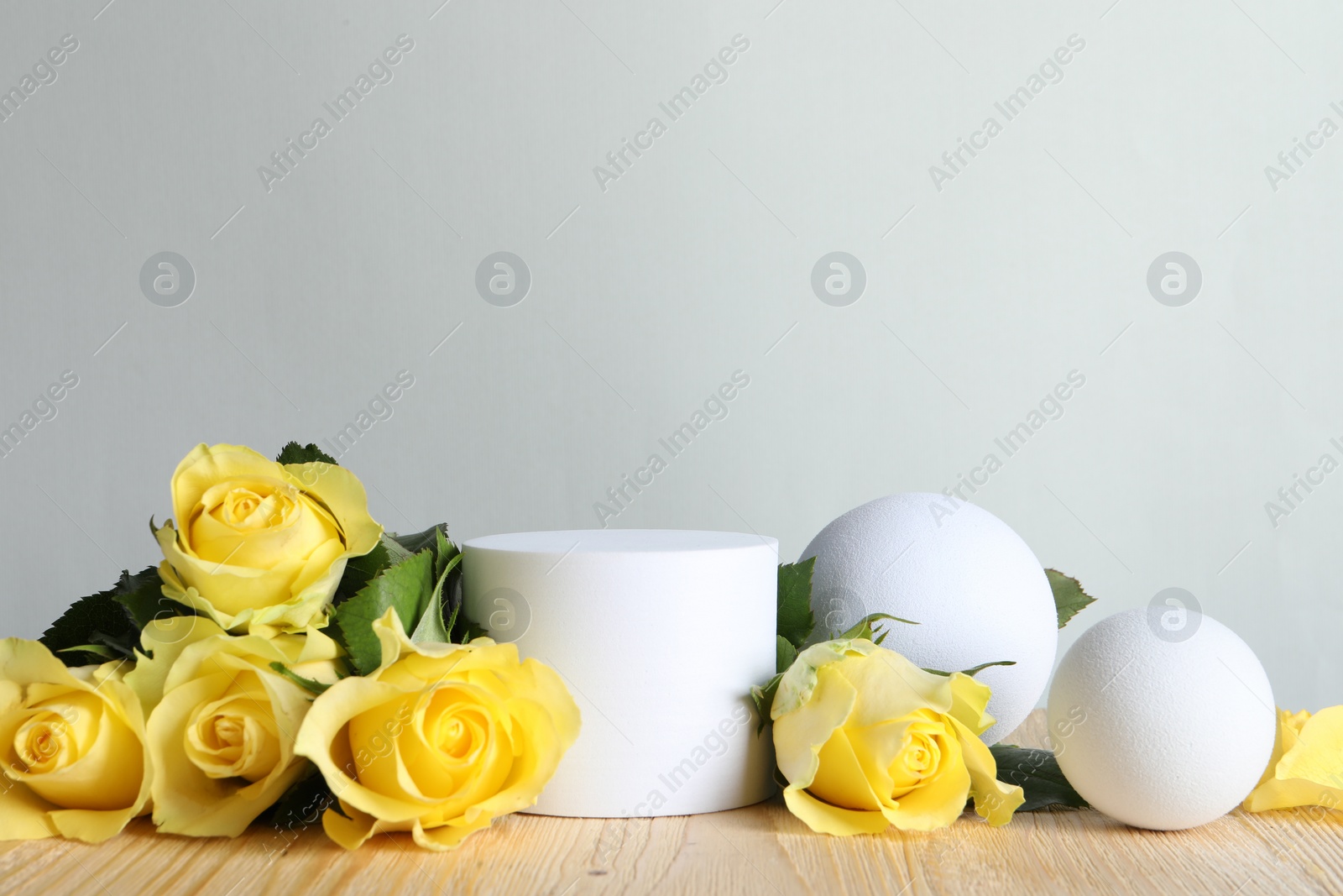 Photo of Beautiful presentation for product. White geometric figures and yellow roses on wooden table against light grey background, space for text