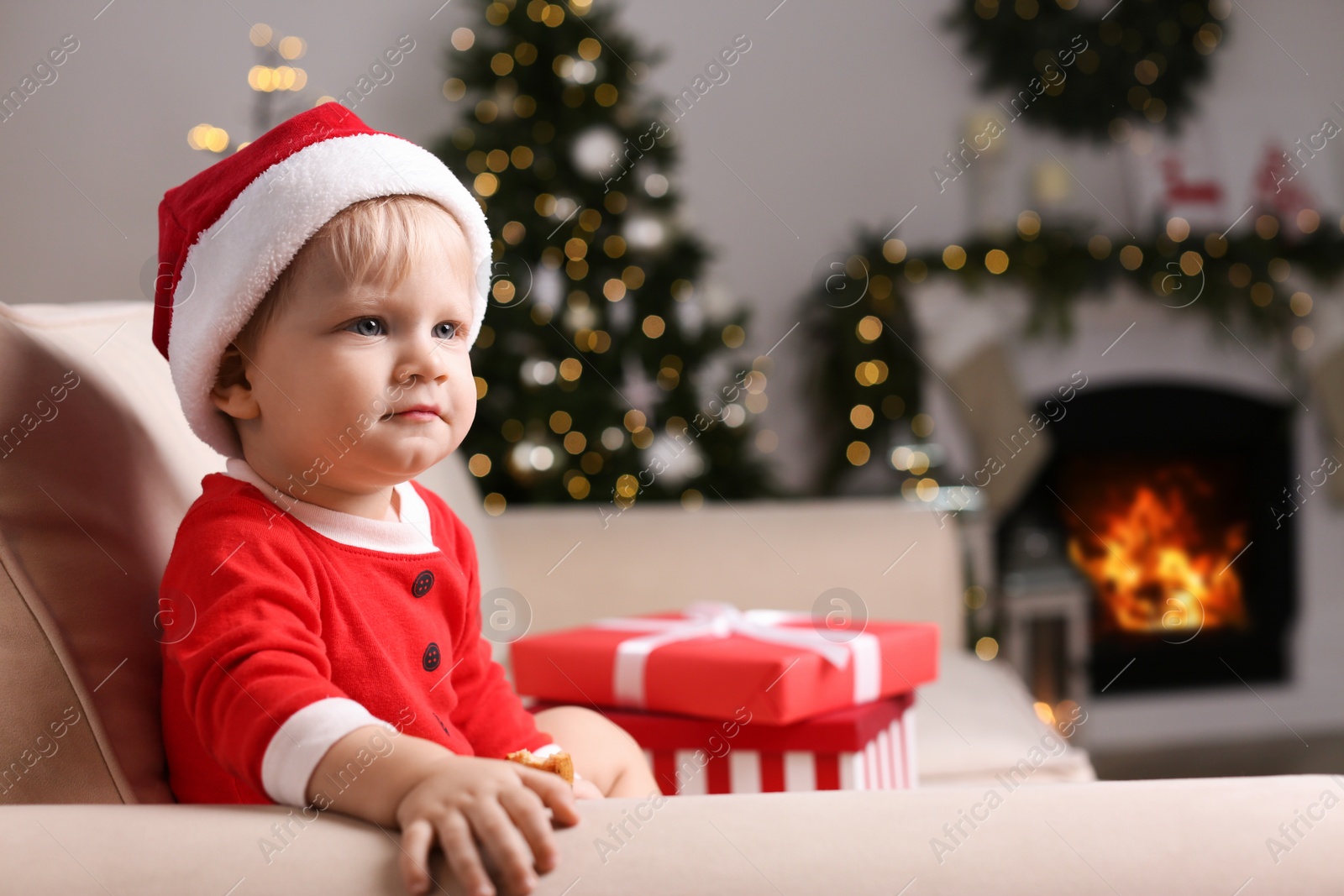 Photo of Baby in cute Christmas outfit eating cookie on sofa at home