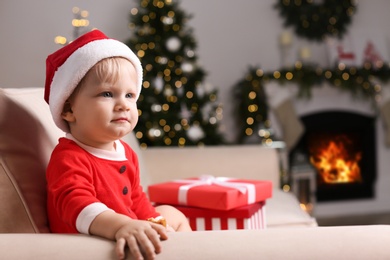 Baby in cute Christmas outfit eating cookie on sofa at home