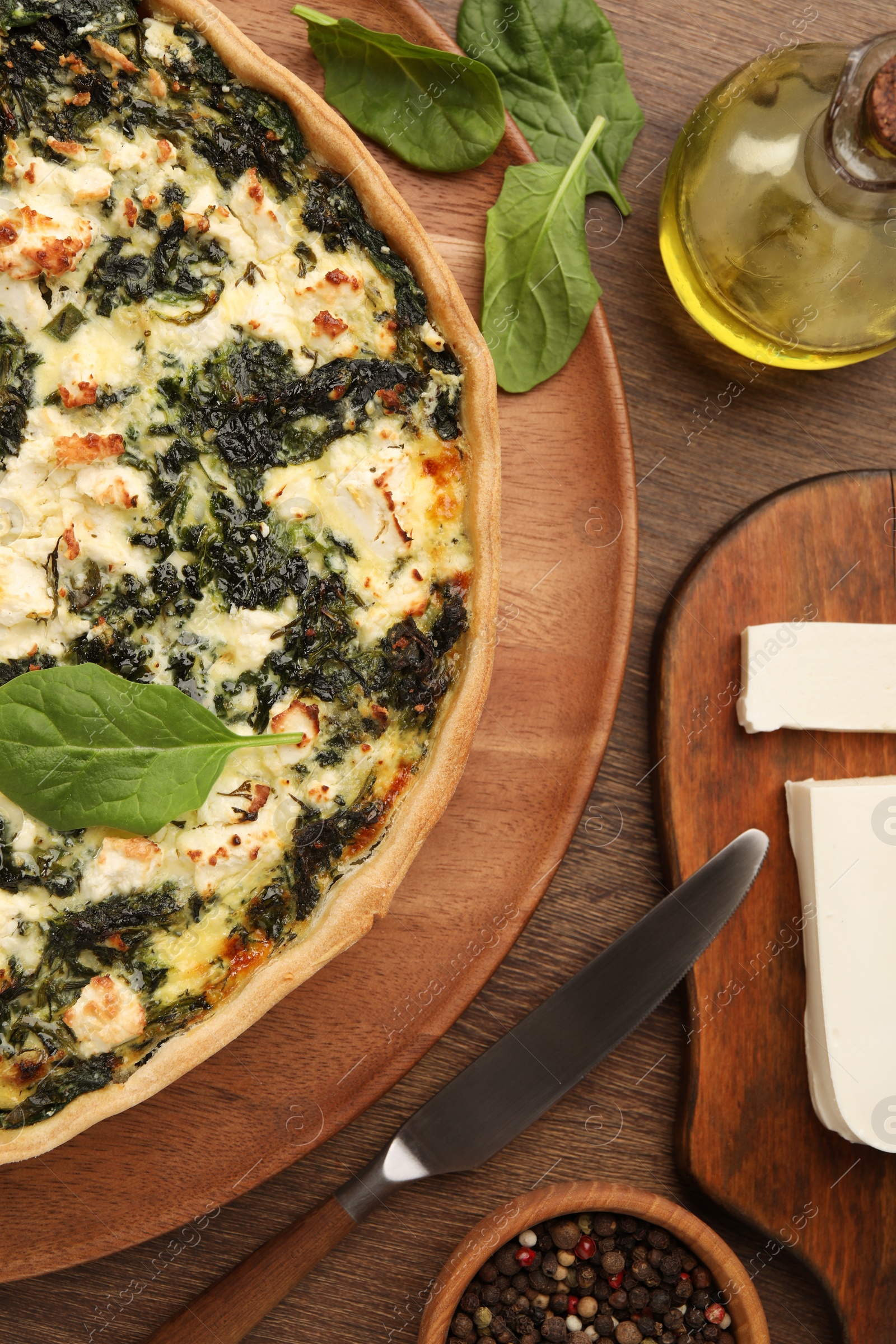 Photo of Delicious homemade spinach quiche, spices and knife on wooden table, flat lay