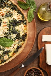 Delicious homemade spinach quiche, spices and knife on wooden table, flat lay