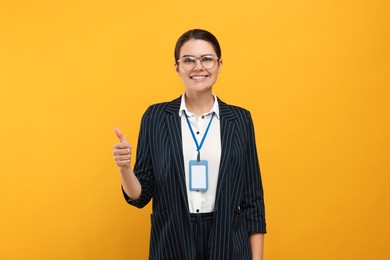Woman with vip pass badge showing thumb up on orange background