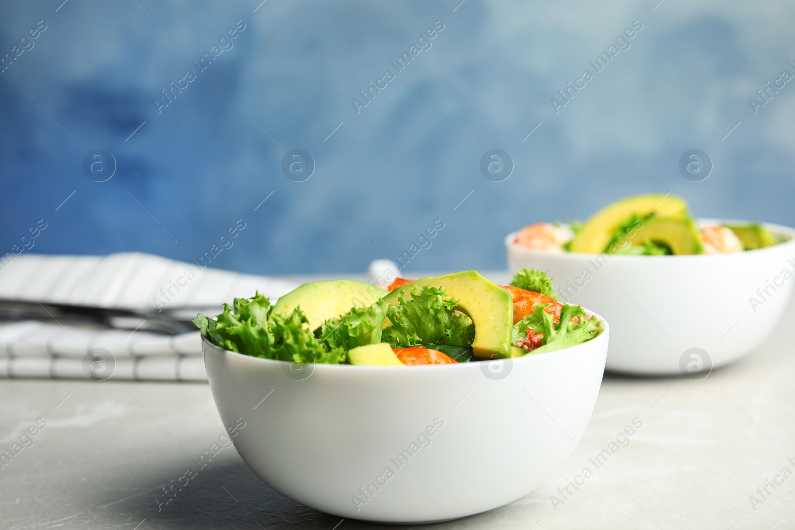 Photo of Delicious avocado salad with shrimps in bowl on grey marble table