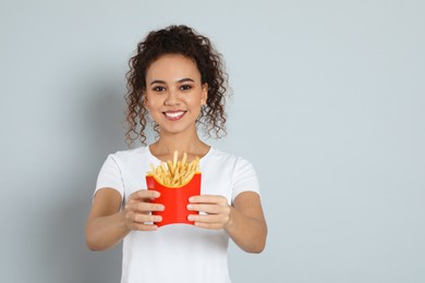 Photo of African American woman with French fries on grey background, space for text