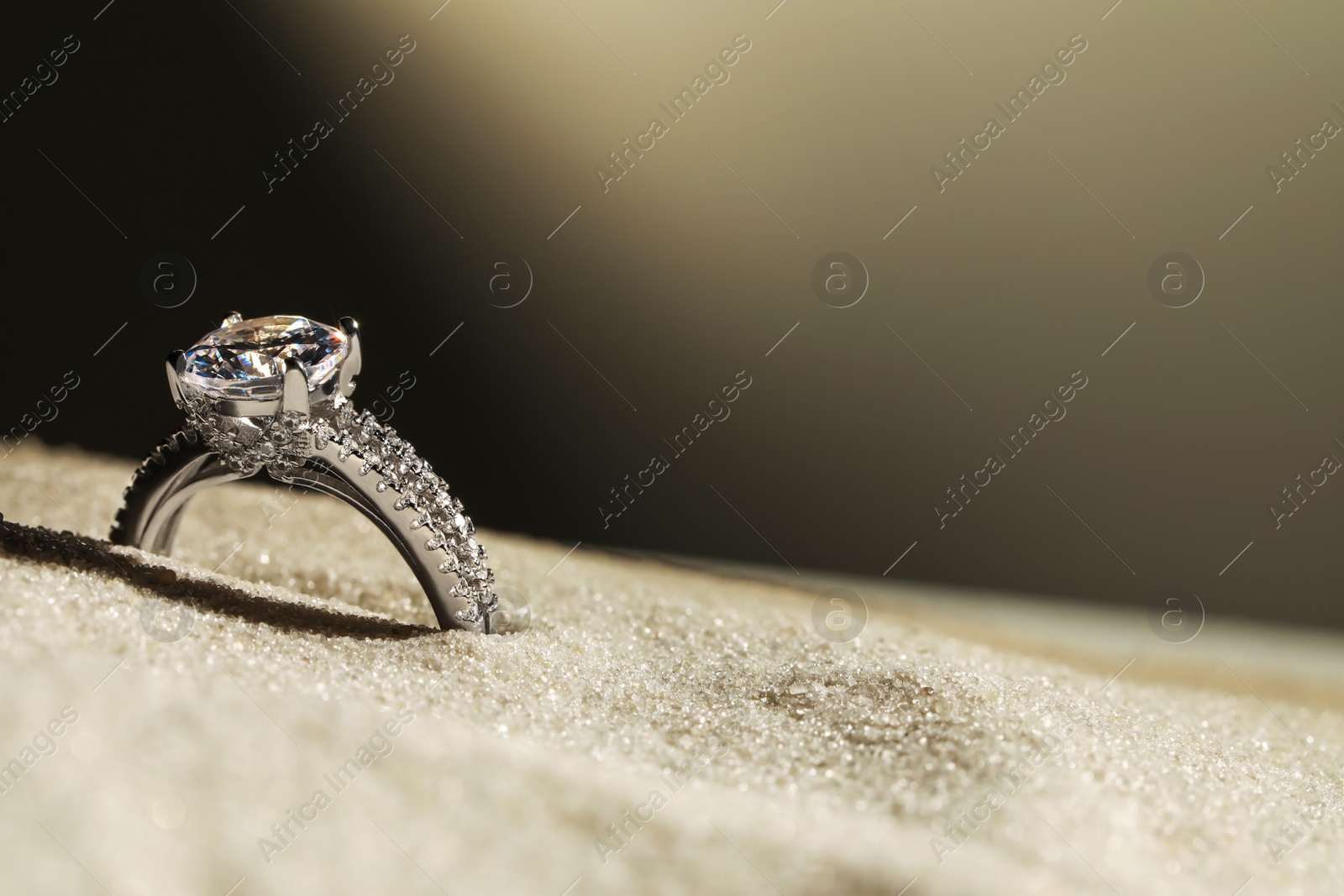 Photo of Luxury jewelry. Stylish presentation of ring in sand against dark background, closeup. Space for text