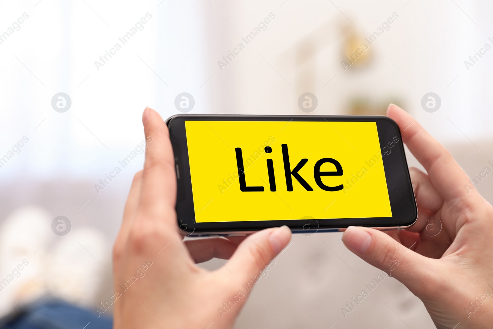 Image of Woman holding smartphone with word Like on screen indoors, closeup