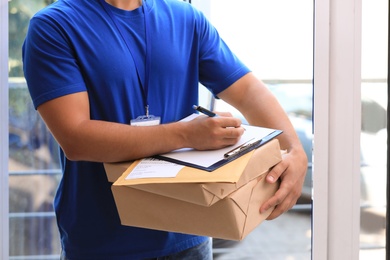 Photo of Young courier with parcels and clipboard on doorstep, closeup. Delivery service