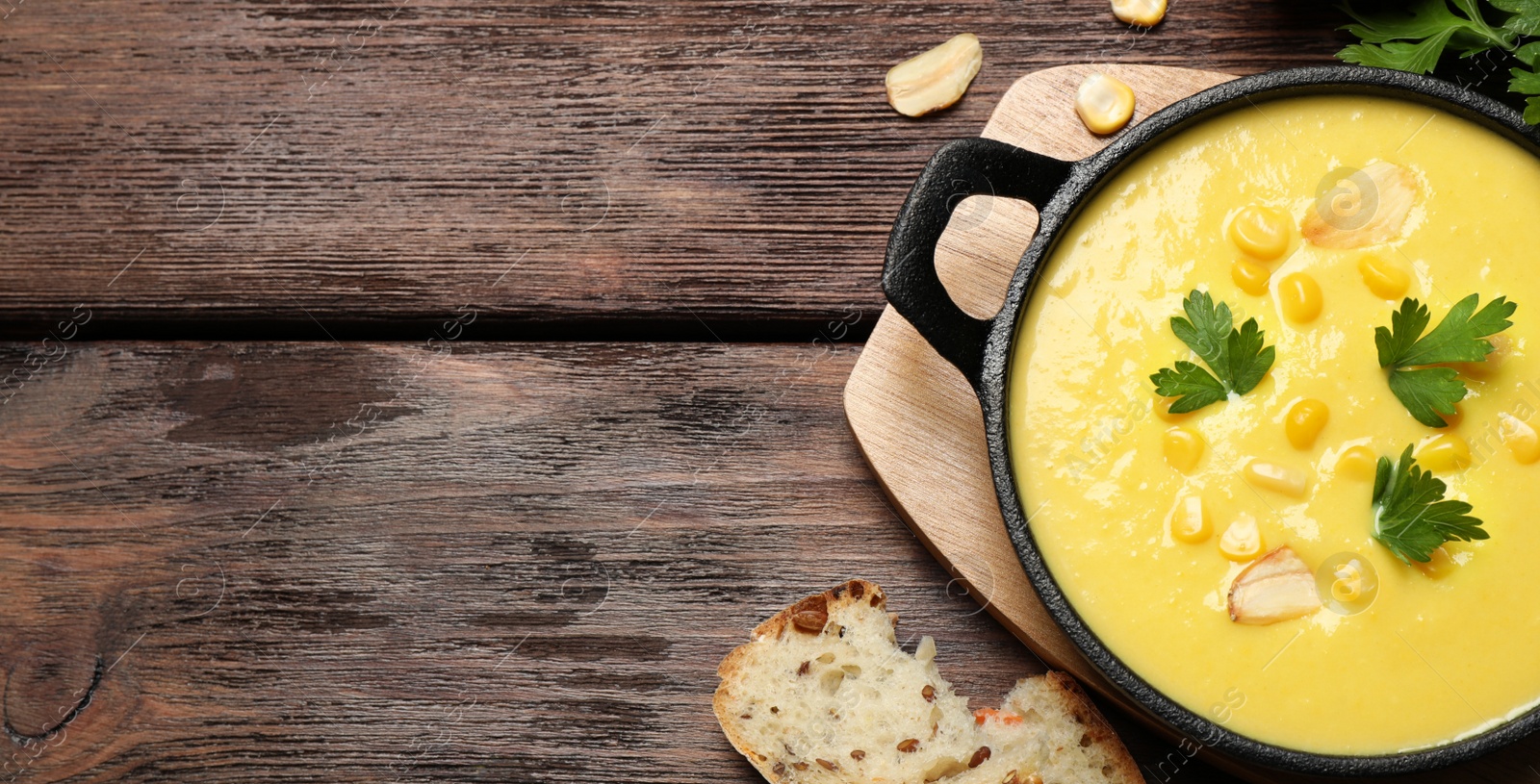 Photo of Delicious creamy corn soup, bread and cob on wooden table, flat lay. Space for text