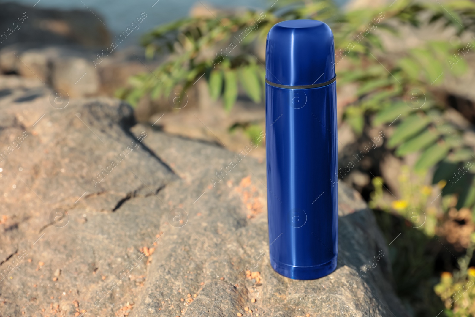 Photo of Modern blue thermos on stone near river. Space for text