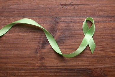 Photo of World Mental Health Day. Green ribbon on wooden background, top view
