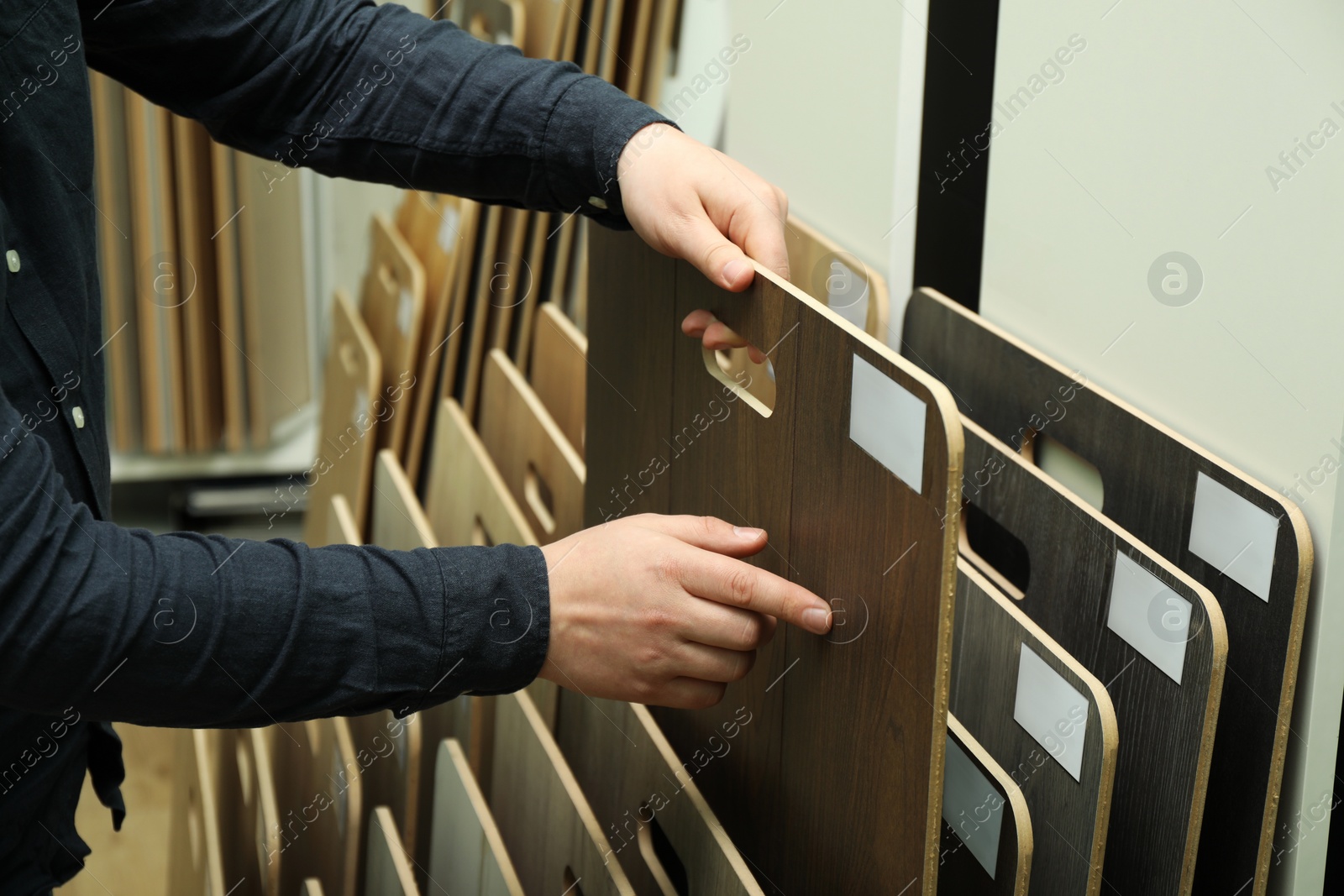 Photo of Man choosing wooden flooring among different samples in shop, closeup