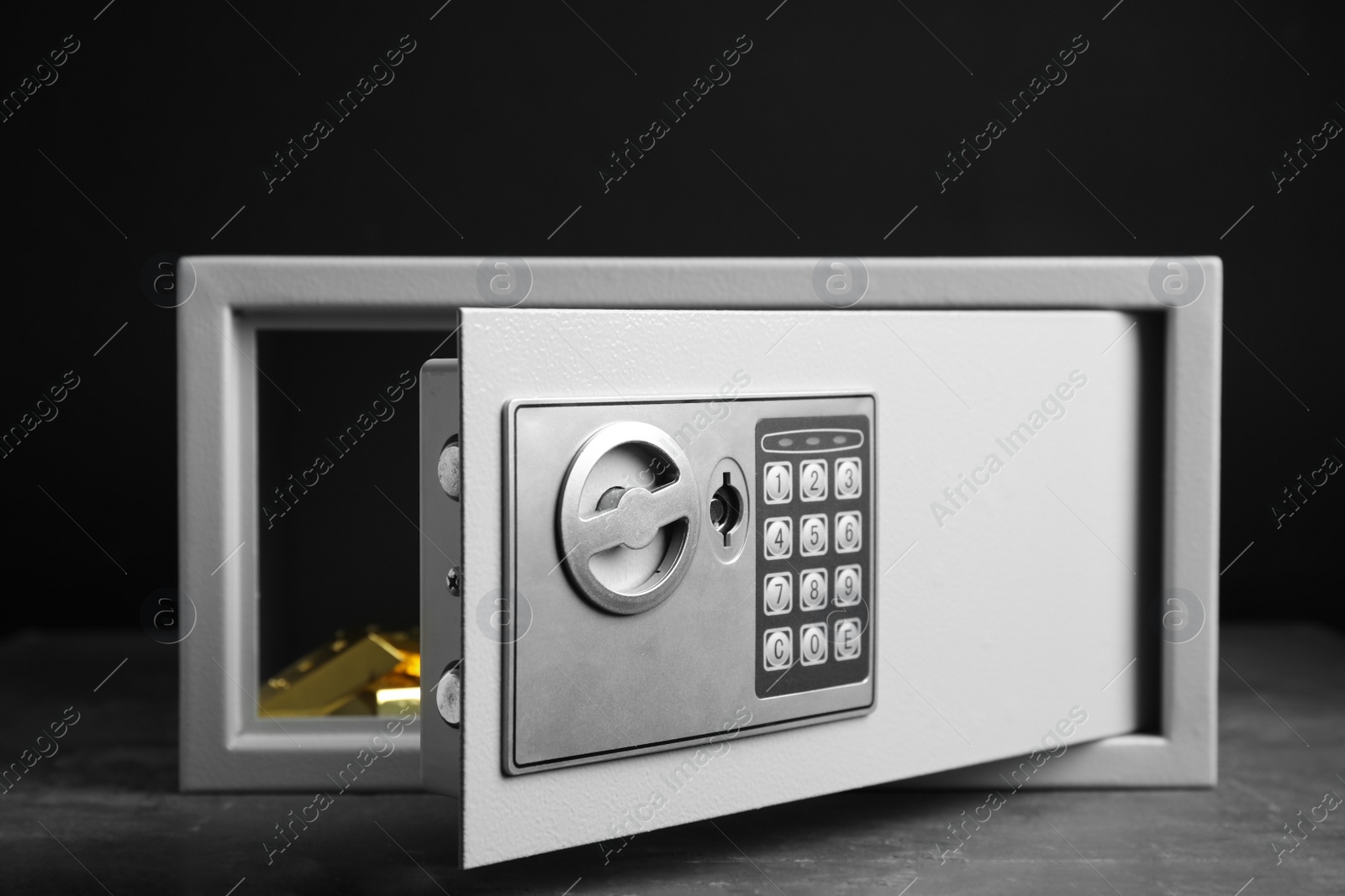 Photo of Open steel safe with gold bars on grey table against black background