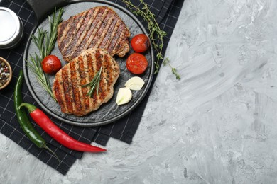 Photo of Delicious grilled pork steaks with spices on gray textured table, top view. Space for text