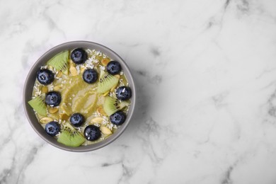 Photo of Bowl of delicious fruit smoothie with fresh blueberries, kiwi slices and coconut flakes on white marble table, top view. Space for text