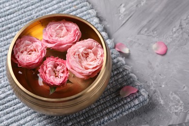 Tibetan singing bowl with water and beautiful roses on grey textured table, above view. Space for text