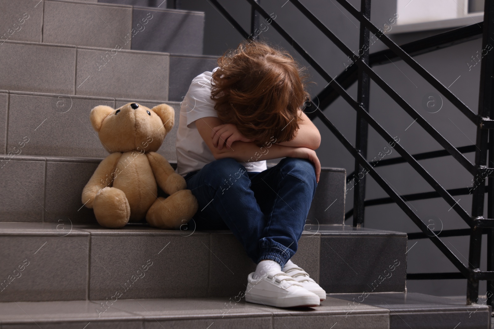 Photo of Child abuse. Upset boy with toy sitting on stairs