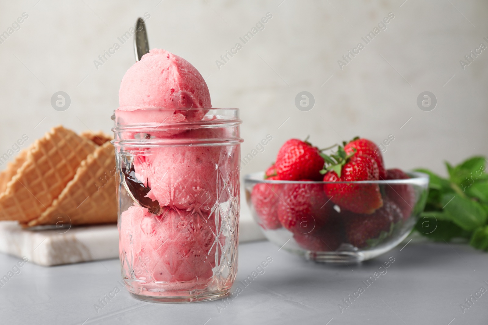 Photo of Delicious pink ice cream served with strawberries on grey table