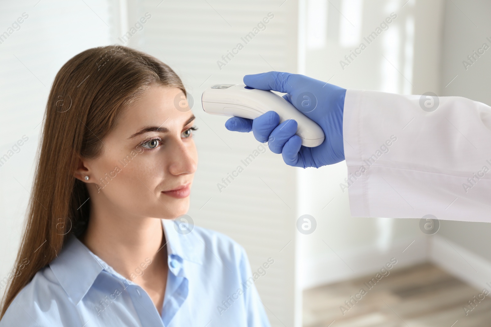 Photo of Doctor measuring patient's temperature with non contact infrared thermometer in office, closeup