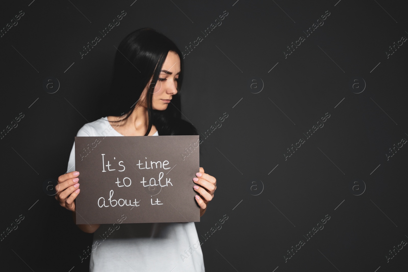 Photo of Young woman holding card with words IT'S TIME TO TALK ABOUT IT against dark background. Space for text