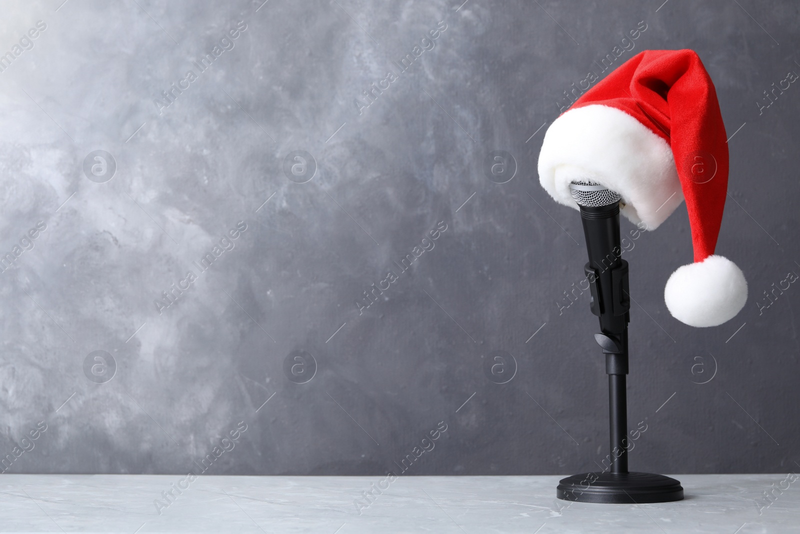 Photo of Microphone with Santa hat on table against grey background, space for text. Christmas music