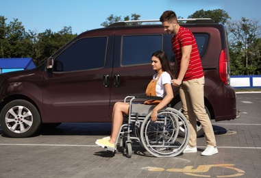 Photo of Young man with woman in wheelchair near van on car parking