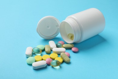 Photo of White bottle and different vitamin pills on light blue background