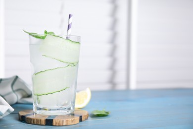 Photo of Glass of refreshing cucumber water with basil on light blue wooden table, space for text