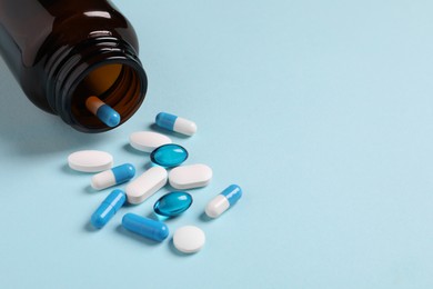 Photo of Plastic bottle with many different pills on light blue background, space for text