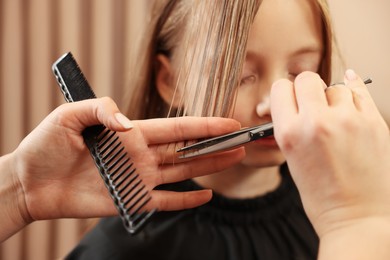 Photo of Professional hairdresser cutting girl's hair in beauty salon, closeup