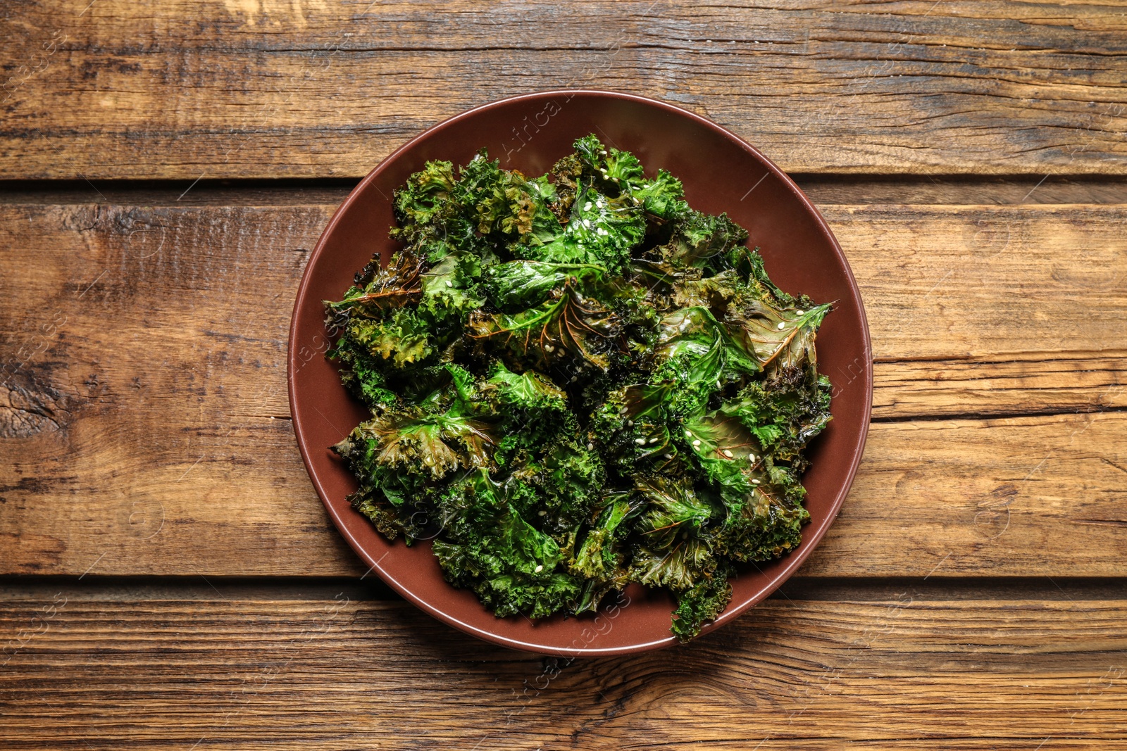 Photo of Tasty baked kale chips on wooden table, top view