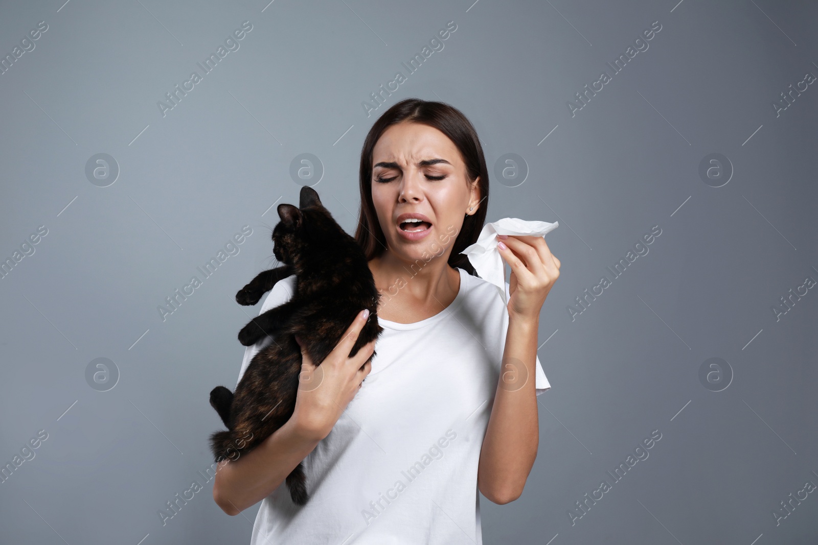 Photo of Young woman with cat suffering from allergy on grey background