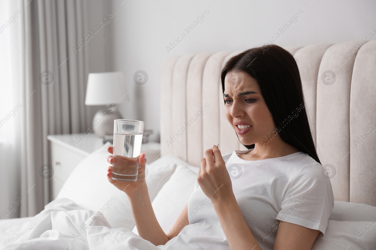 Photo of Young woman taking medication for migraine in bed at home