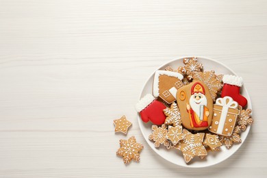 Photo of Tasty gingerbread cookies on white wooden table, flat lay with space for text. St. Nicholas Day celebration