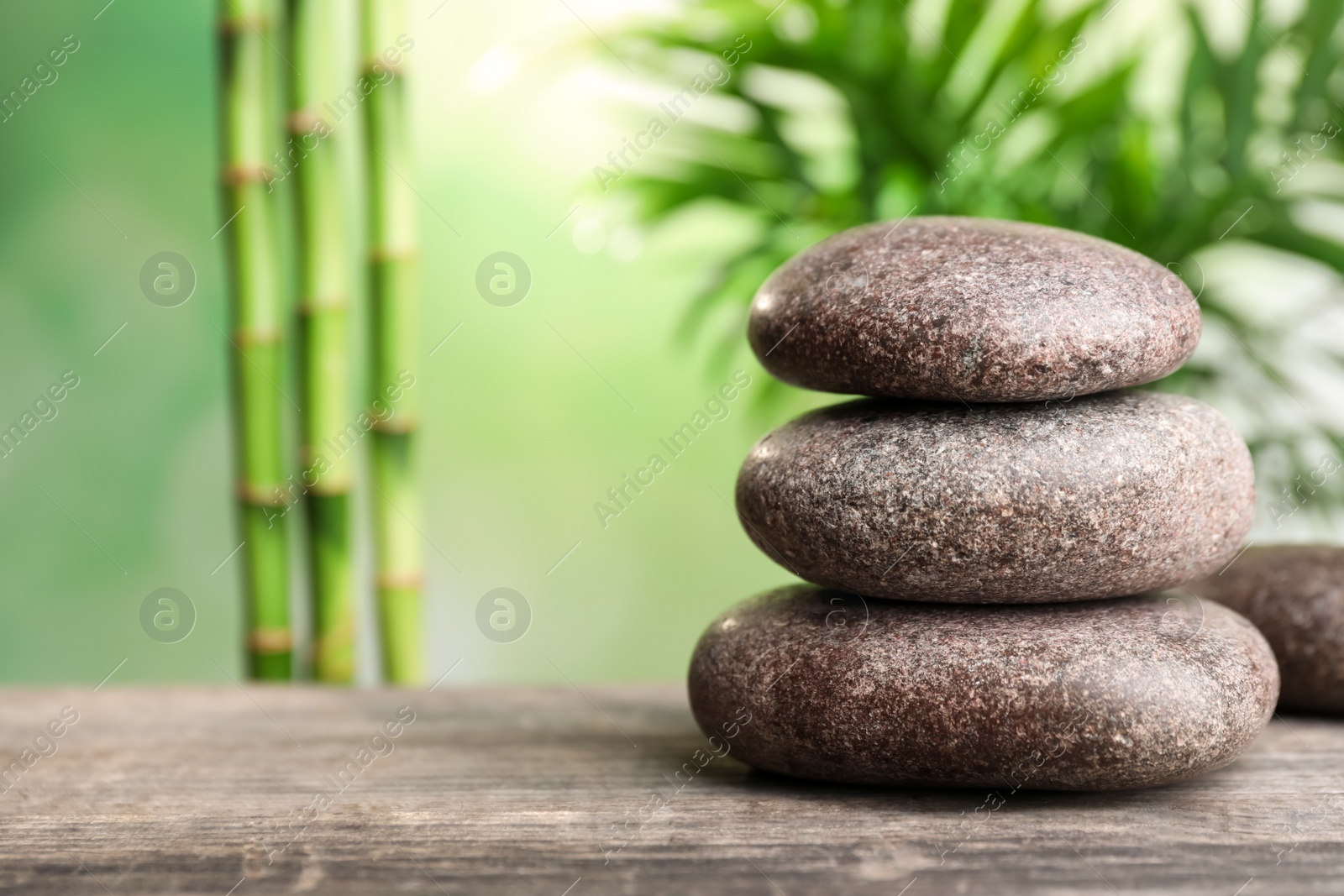 Photo of Stacked spa stones on wooden table against bamboo stems and green leaves. Space for text