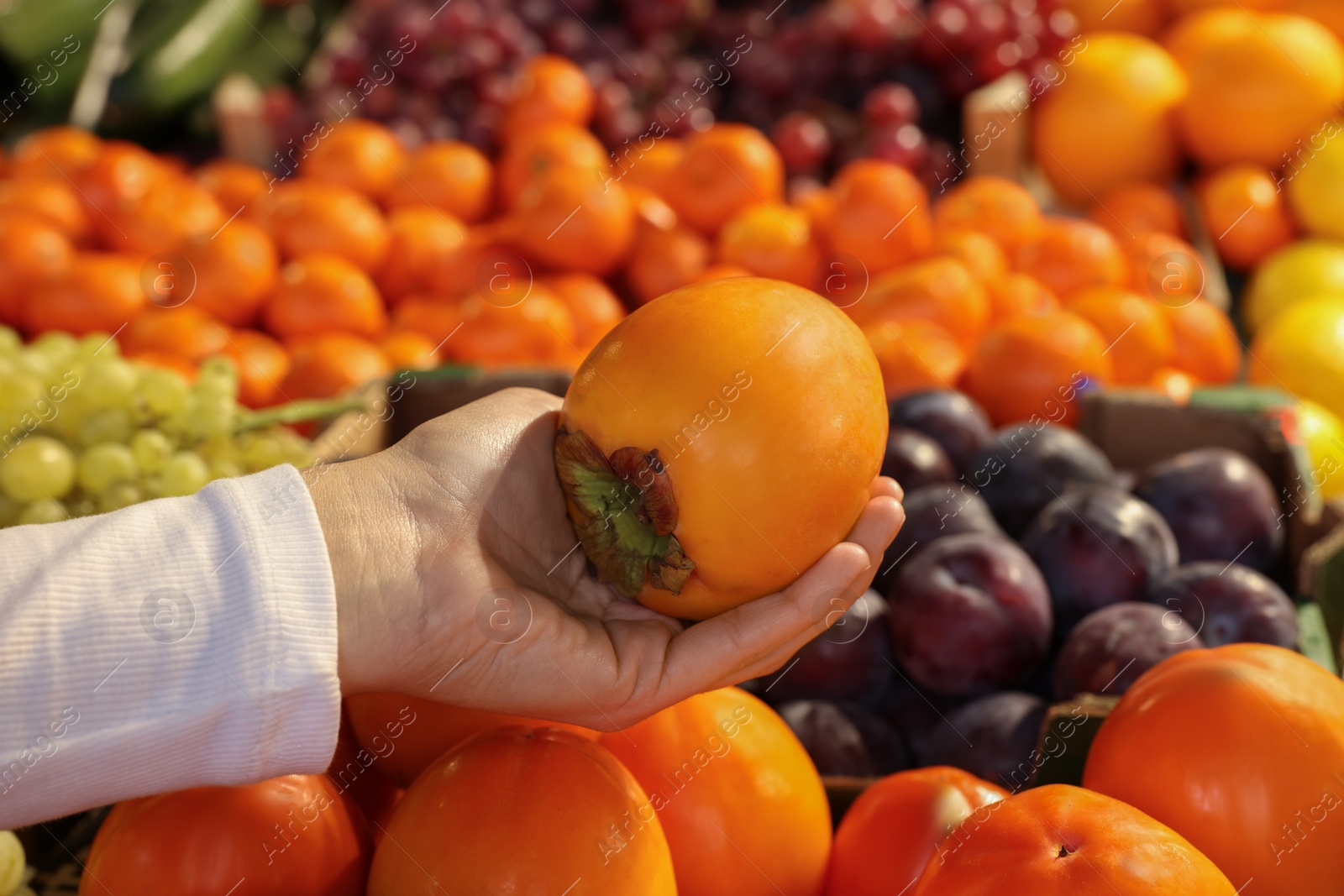 Photo of Woman holding fresh persimmon near fruit counter at market, closeup