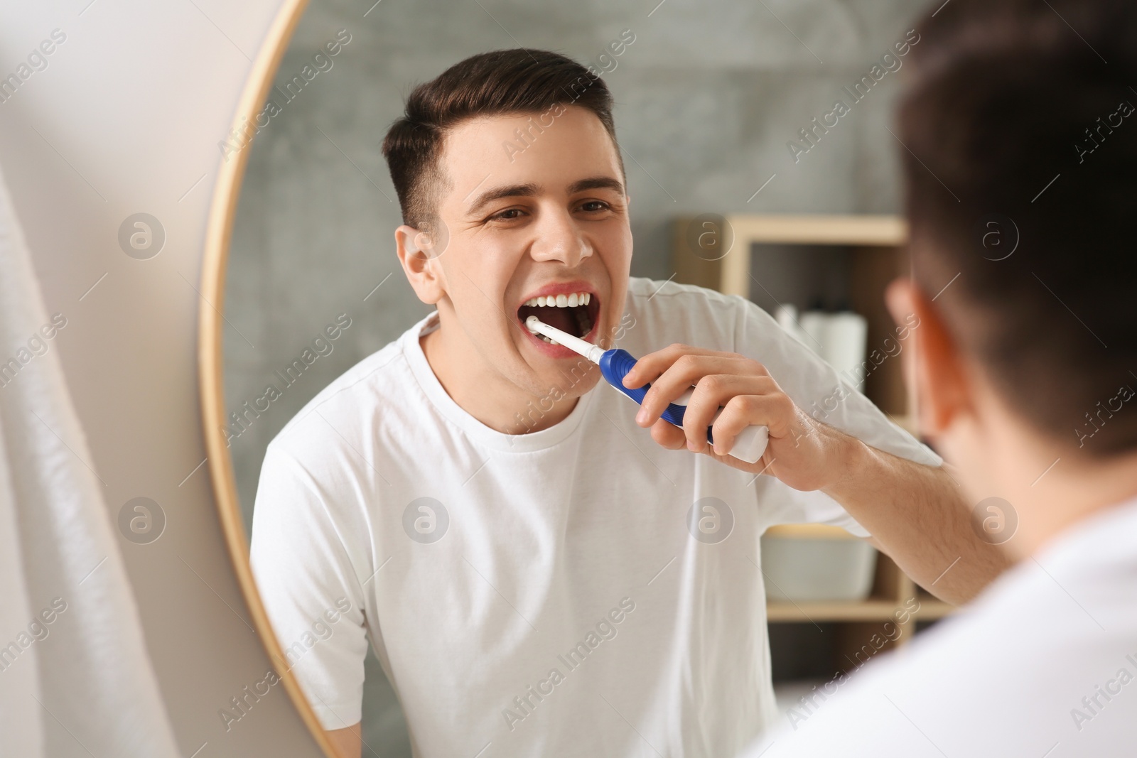 Photo of Man brushing his teeth with electric toothbrush near mirror in bathroom