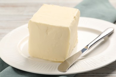 Photo of Block of tasty butter and knife on white wooden table, closeup