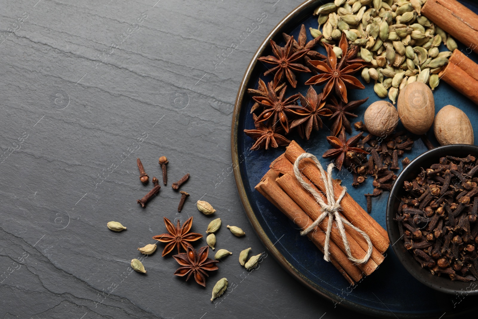 Photo of Dishware with different spices and nuts on gray table, top view. Space for text