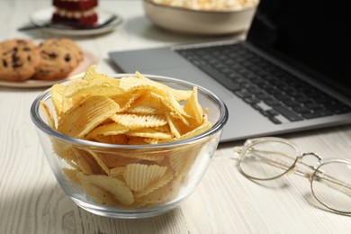Photo of Bad eating habits at workplace. Tasty ridged chips in bowl on white wooden table, closeup