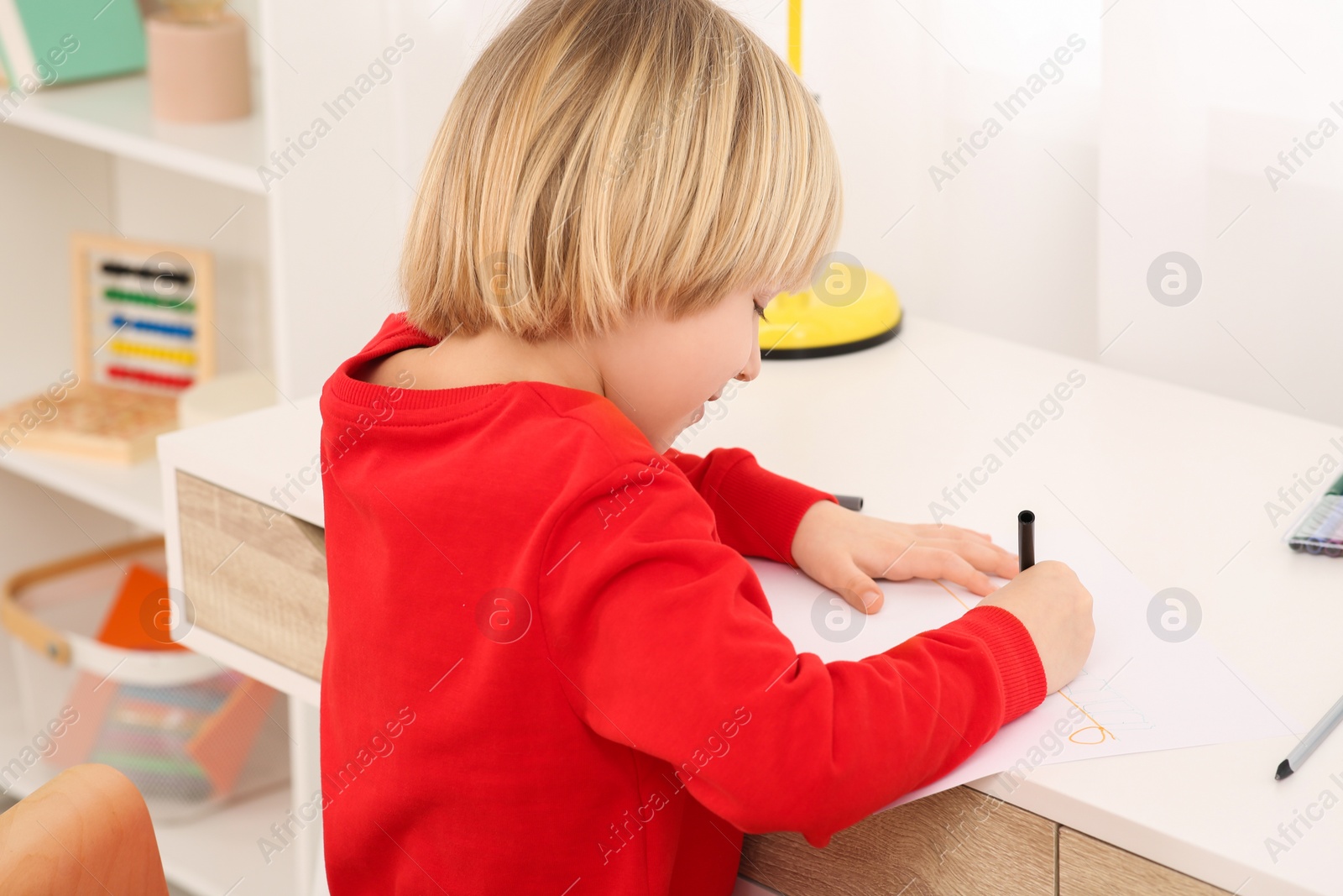 Photo of Cute little boy drawing with marker at desk in room, closeup. Home workplace