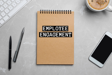 Notebook with text EMPLOYEE ENGAGEMENT and smartphone on grey table, flat lay
