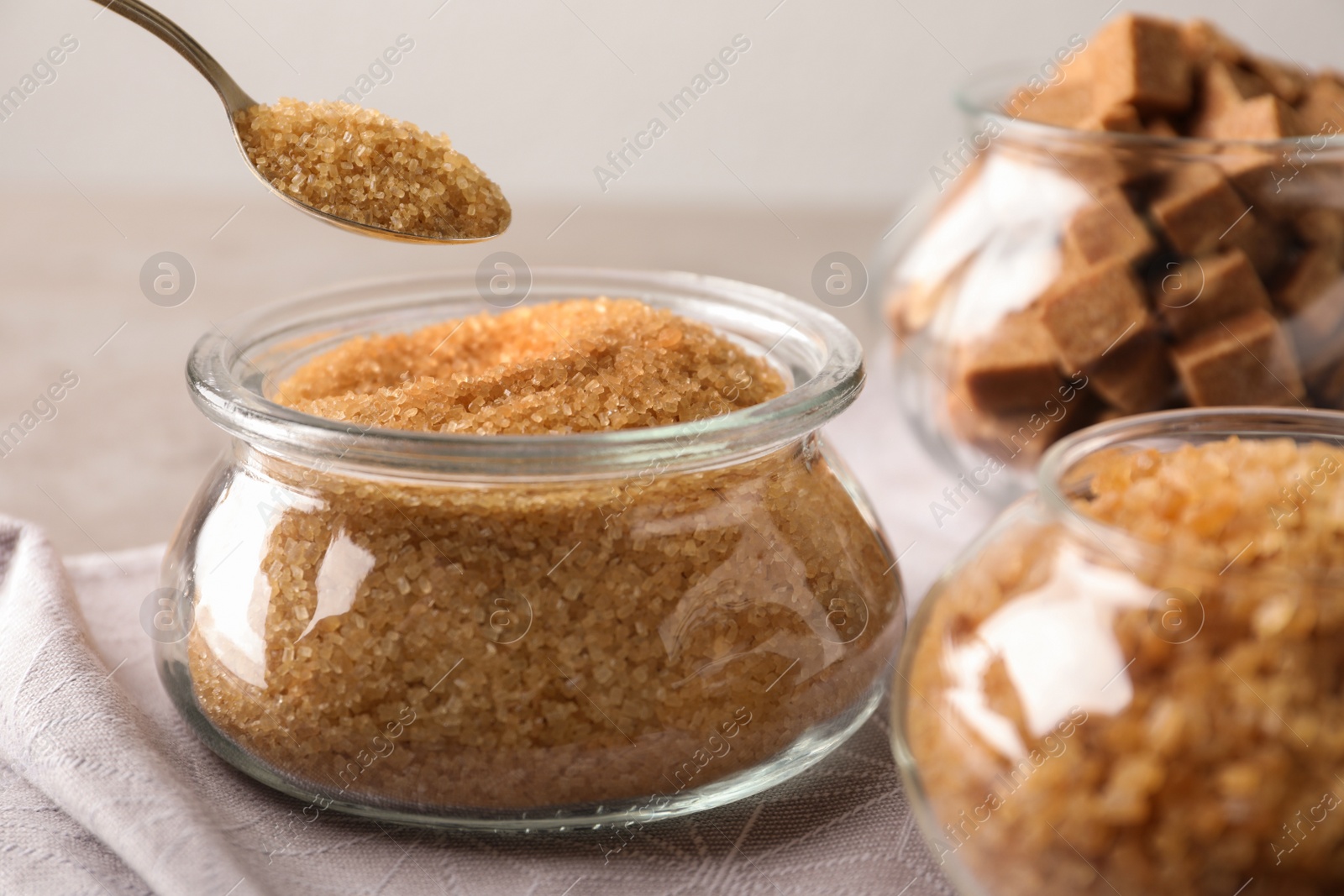 Photo of Taking spoon of brown sugar from glass bowl on table