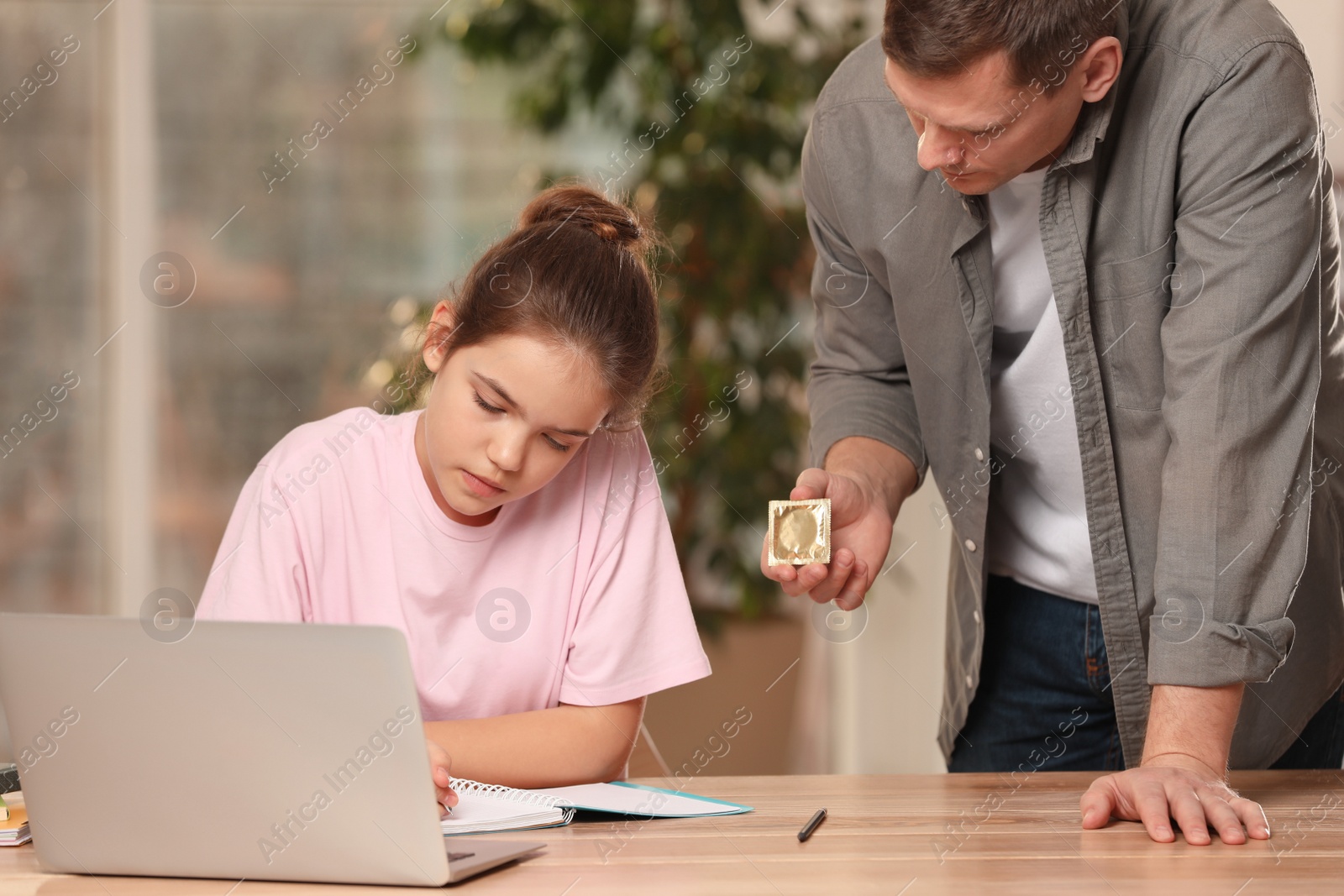 Photo of Father talking with his teenage daughter about contraception while she using laptop at home. Sex education concept