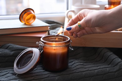 Photo of Woman lighting beautiful candle near window indoors, closeup