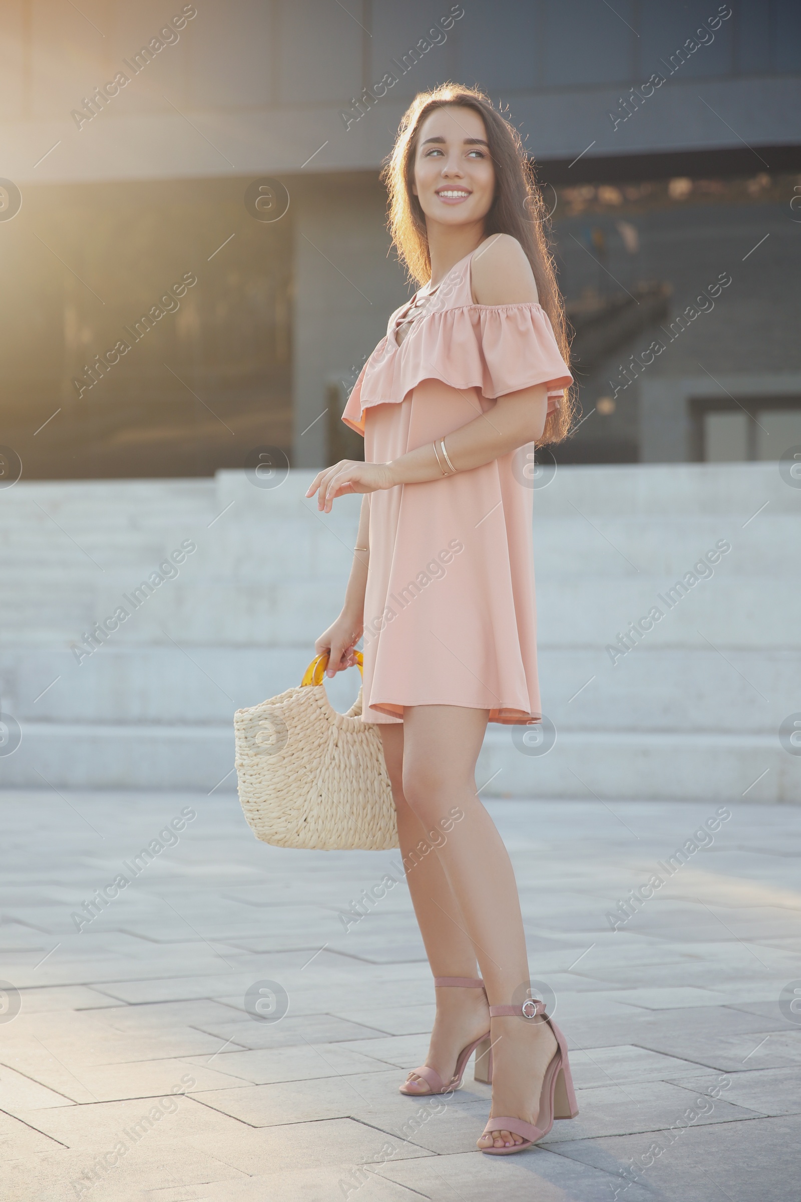 Photo of Beautiful young woman in stylish pink dress with handbag on city street